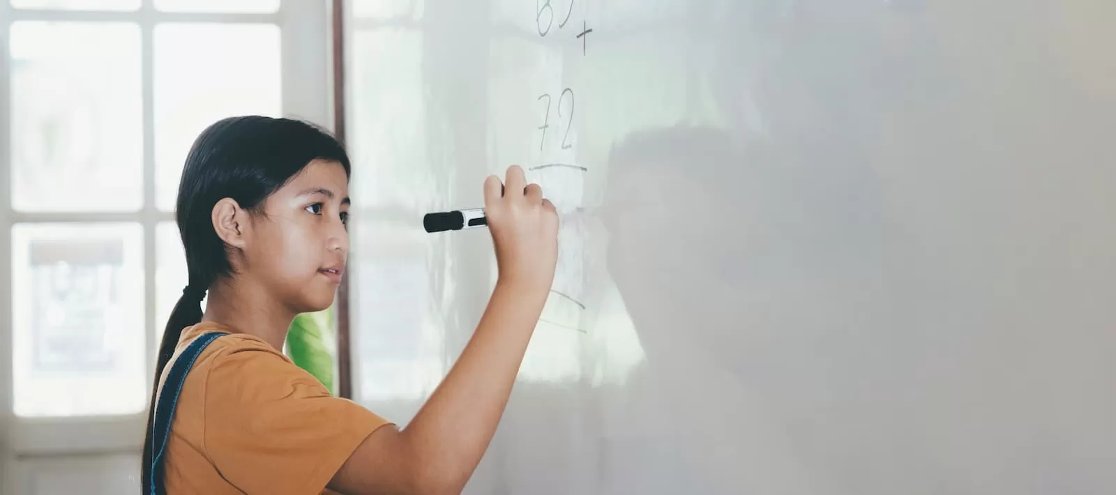 alumna joven con coleta resuelve ejercicio de matemática en pizarra blanca